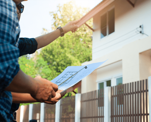 Male Contractor holding blueprint and ruler pointing to house exterior with another male client. Structur Residential Construction Consulting